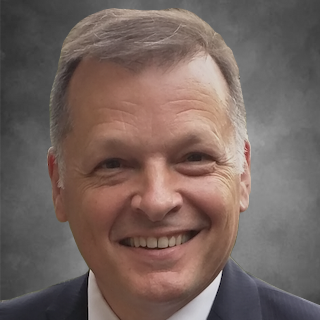 A man in a suit and white shirt is smiling for the camera.