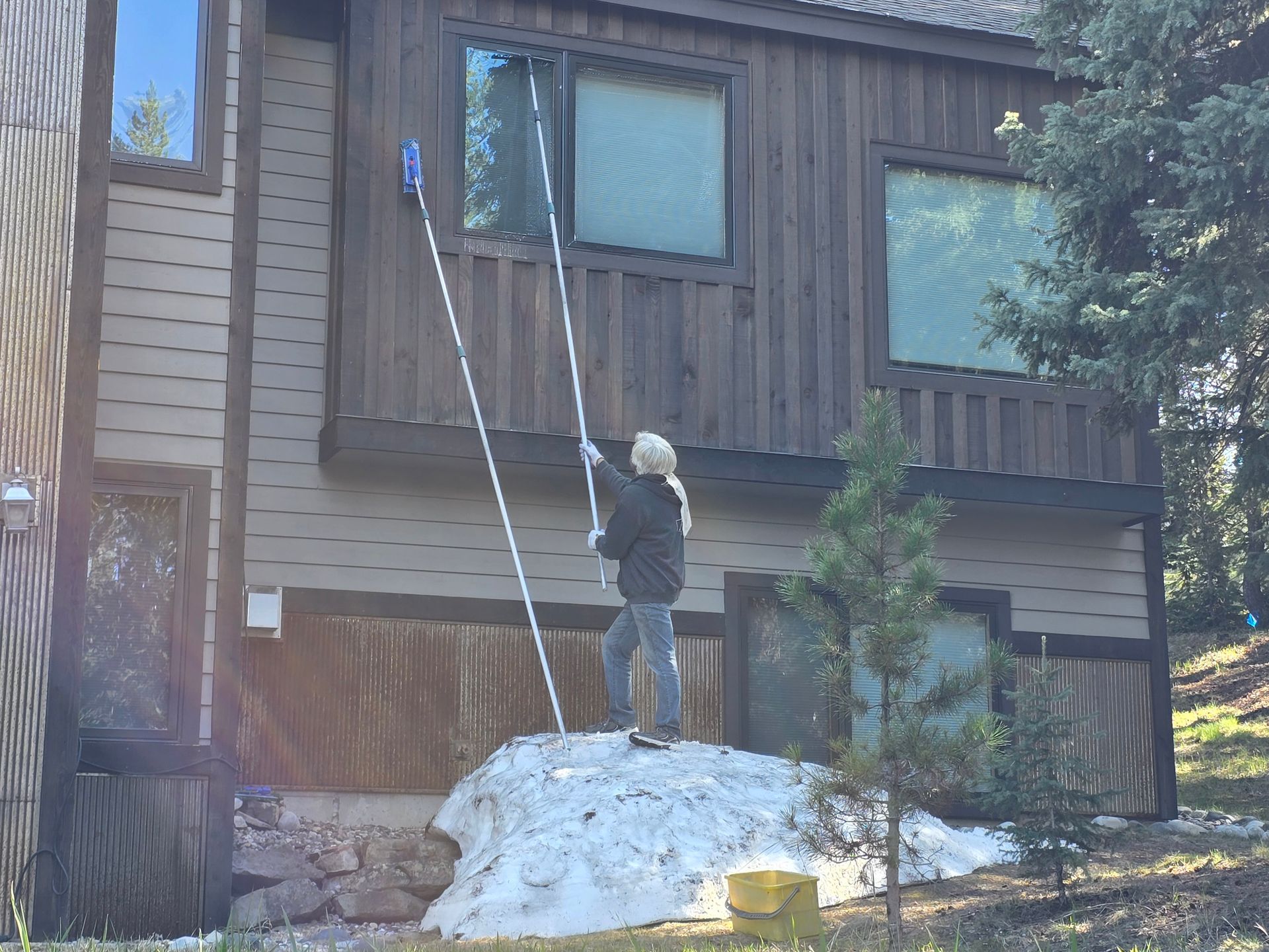 A woman is cleaning the windows of a house with a mop.