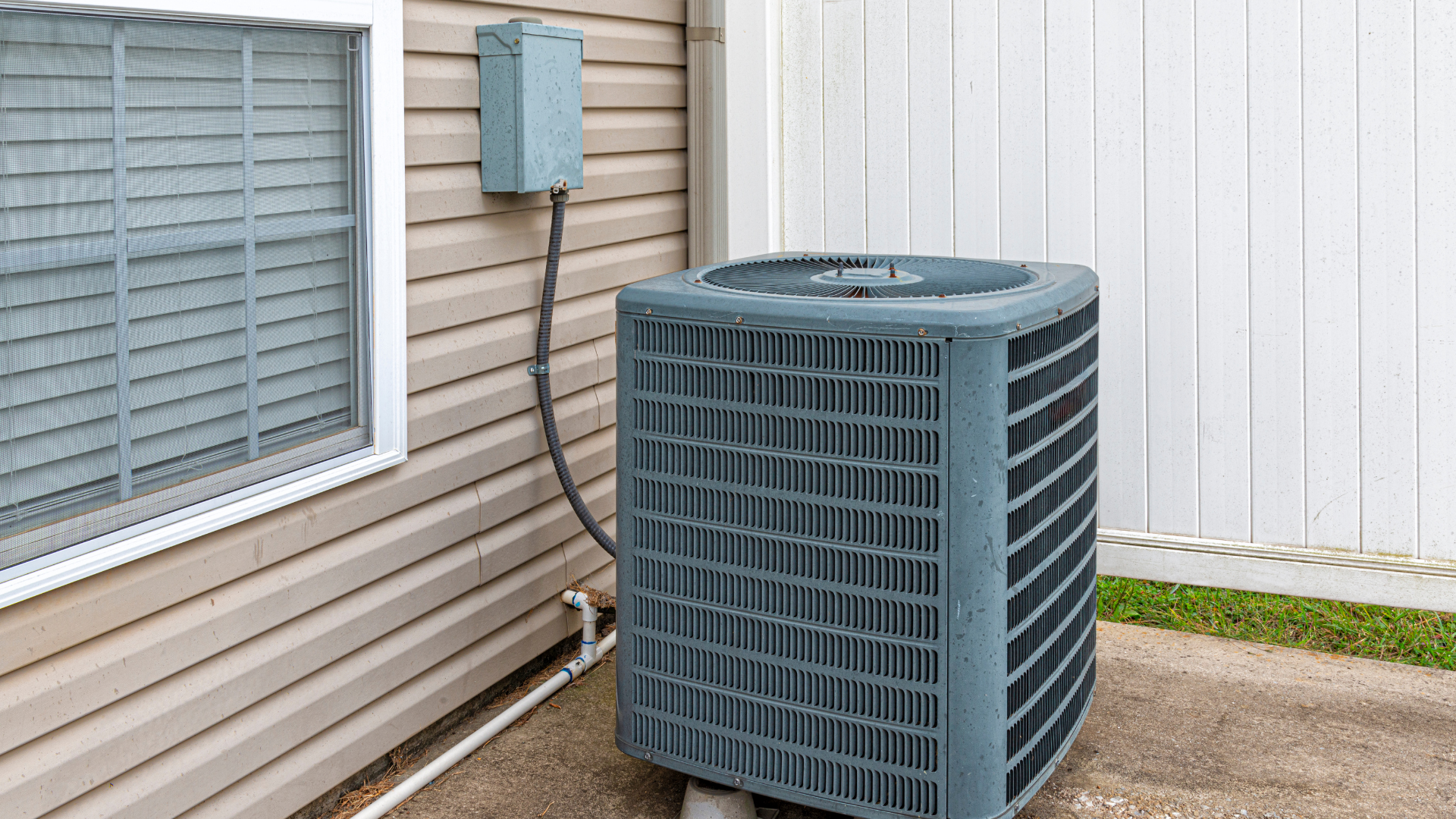 An air conditioner is sitting on the side of a house next to a window.