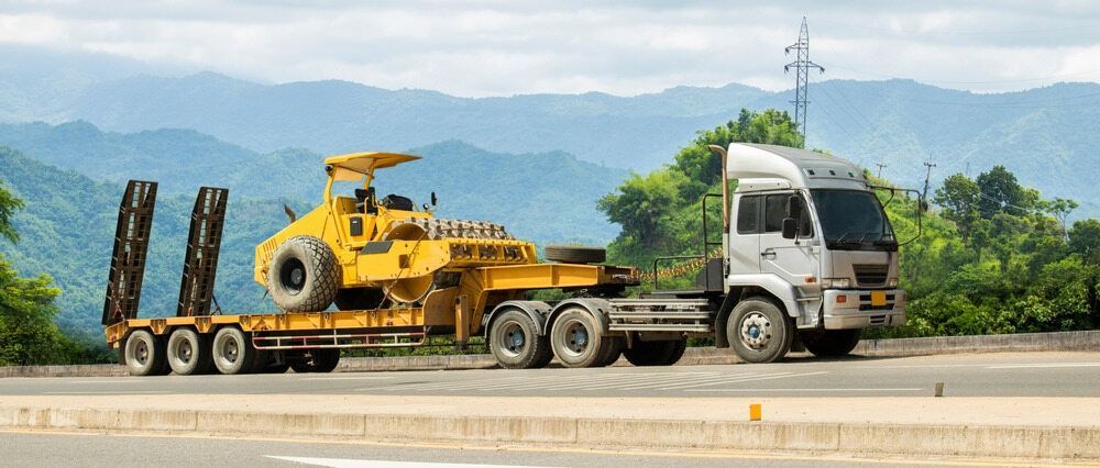 A Truck Is Carrying A Yellow Bulldozer On A Trailer On A Highway — RJN Transport In Tamworth, NSW
