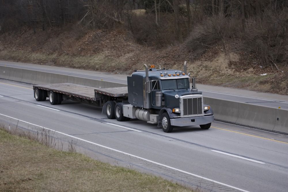 A Semi Truck With A Flatbed Trailer Is Driving Down A Highway — RJN Transport In Inverell, NSW