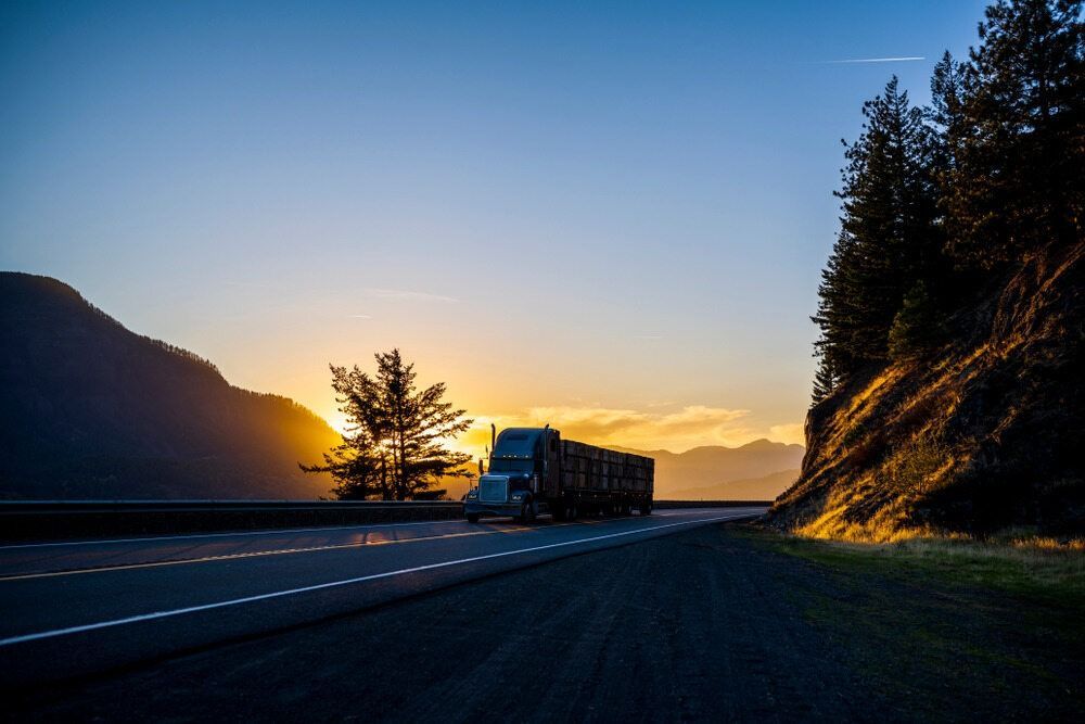 A Semi Truck Is Driving Down A Highway At Sunset — RJN Transport In Coonabarabran, NSW
