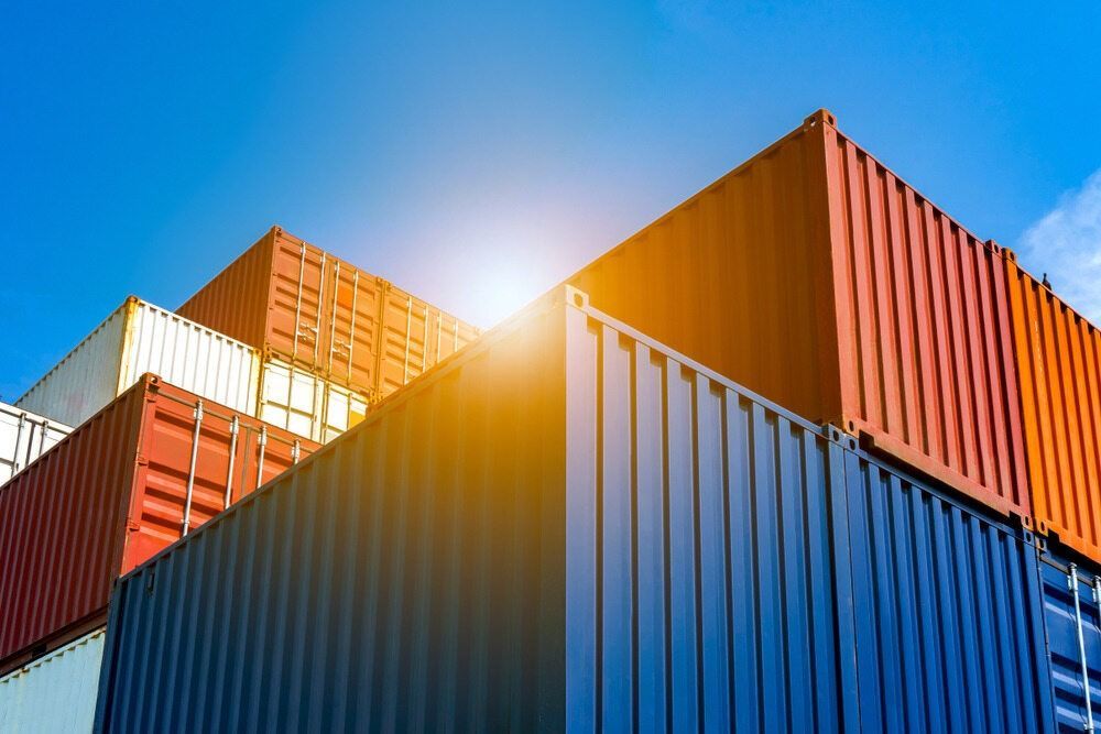 A Stack Of Shipping Containers Against A Blue Sky With The Sun Shining Through Them — RJN Transport In Inverell, NSW
