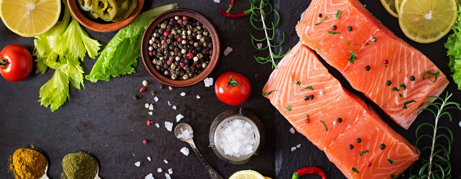 Dos trozos de salmón rodeados de verduras y especias sobre una mesa.