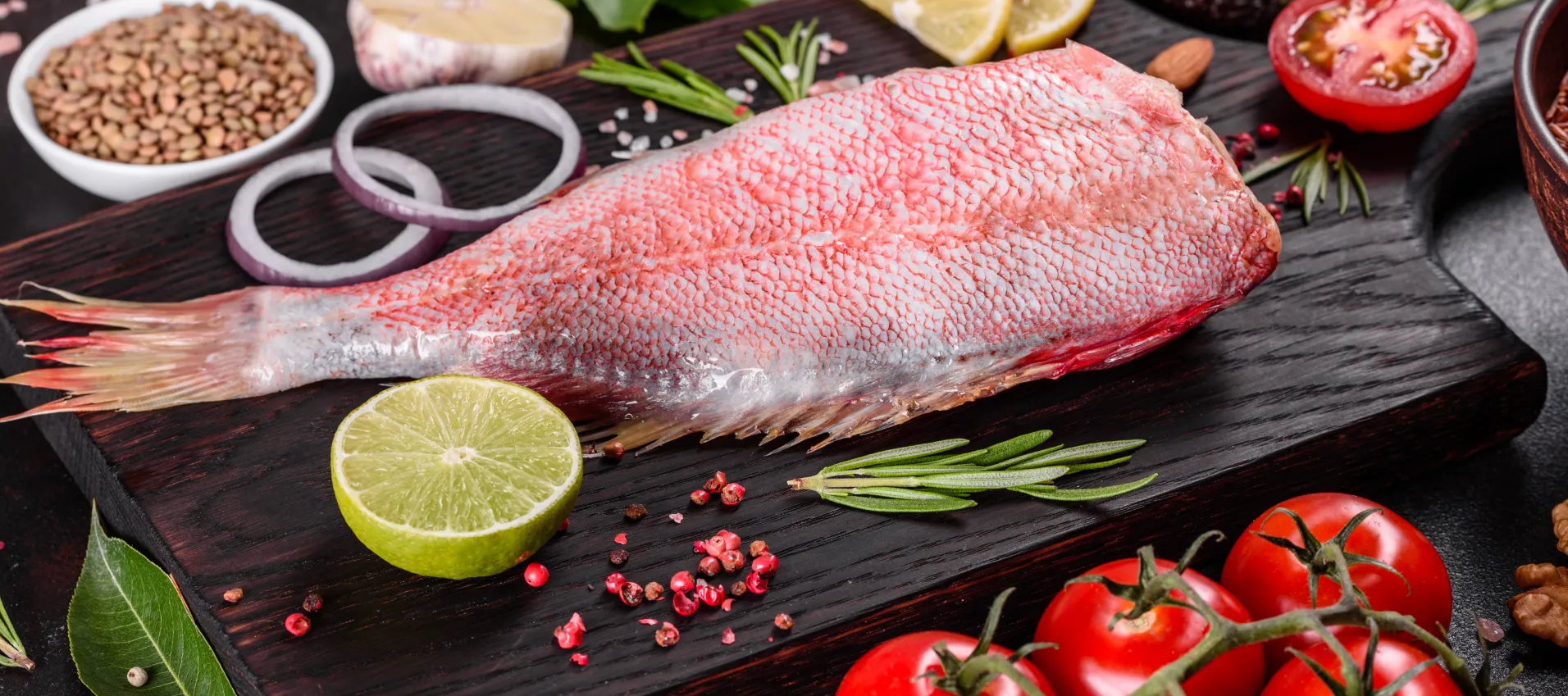 Un pescado está sentado sobre una tabla de cortar de madera rodeado de verduras y especias.