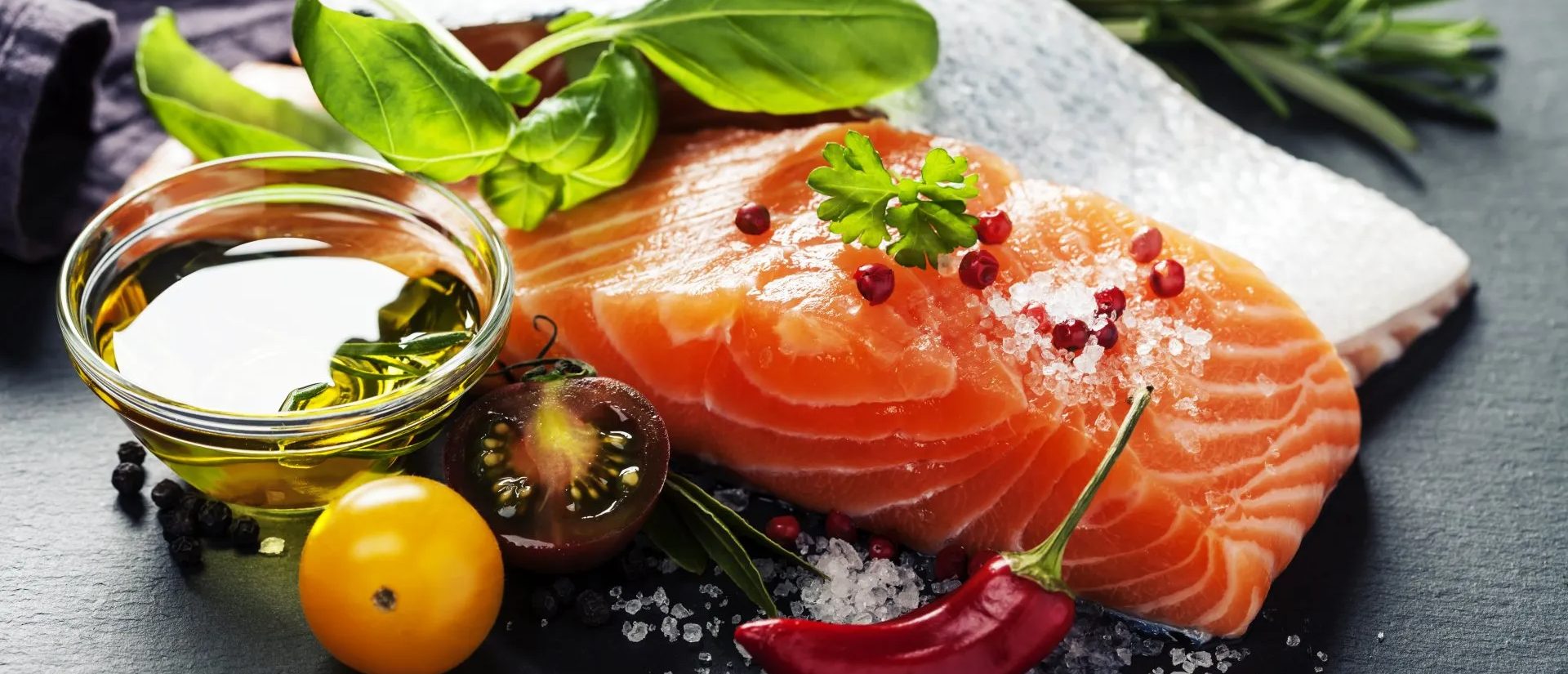 Un trozo de salmón se rodea de verduras y un bol de aceite.