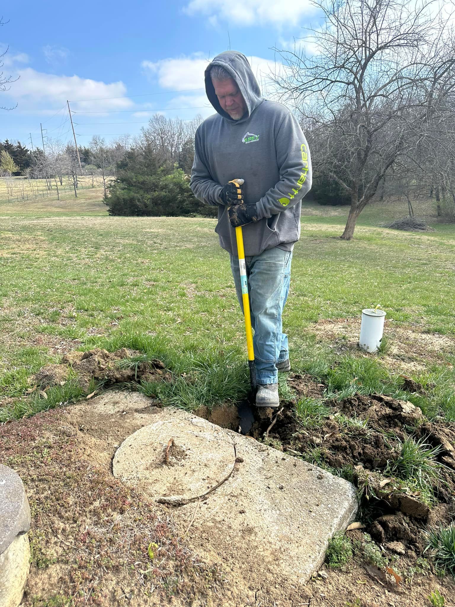 A man is digging a hole in the ground next to a tree stump.