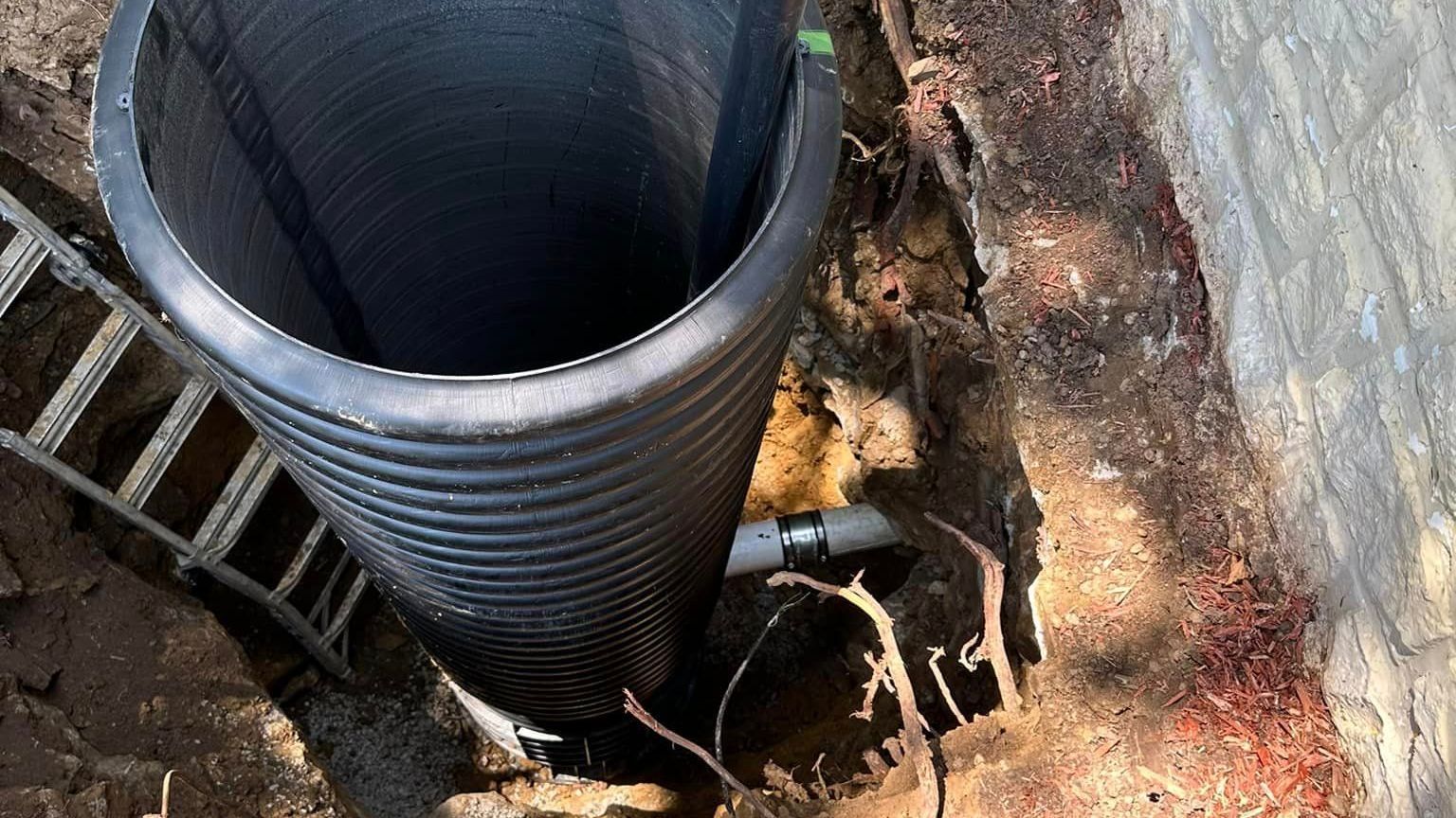 A large black pipe is sitting in the dirt next to a ladder.