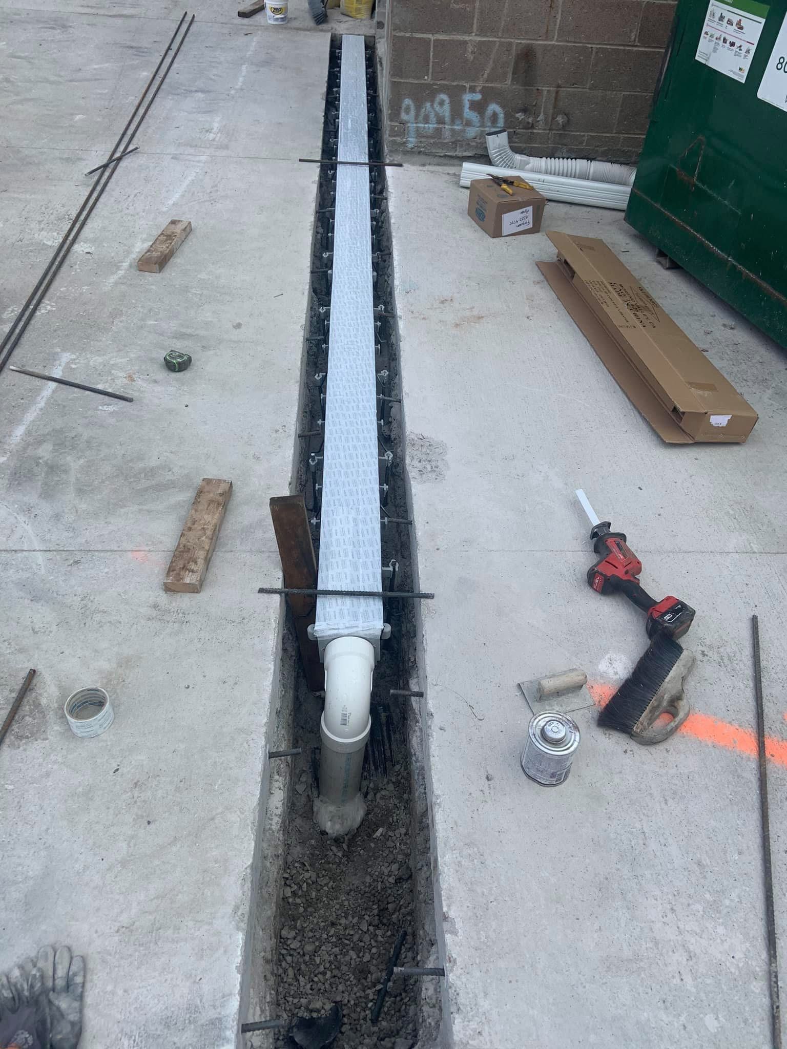 A drain pipe is being installed in a concrete trench.