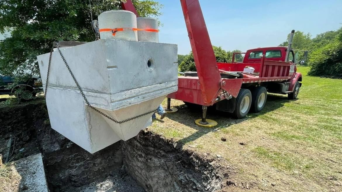 A red truck is carrying a large concrete block in the dirt.