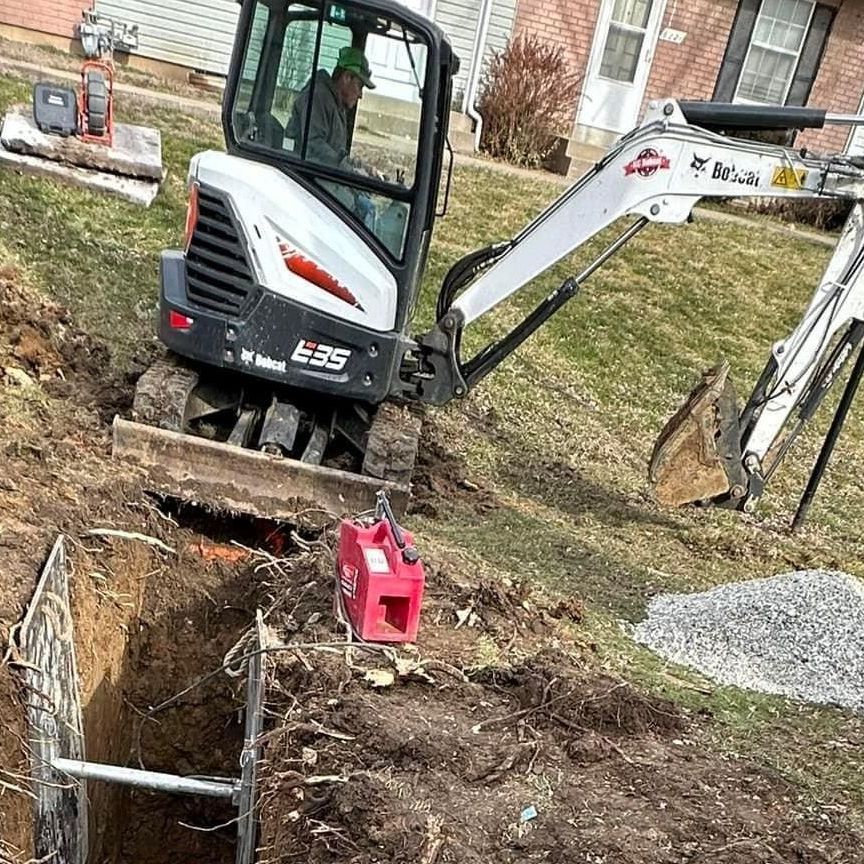 A small excavator is digging a hole in the ground in front of a house.