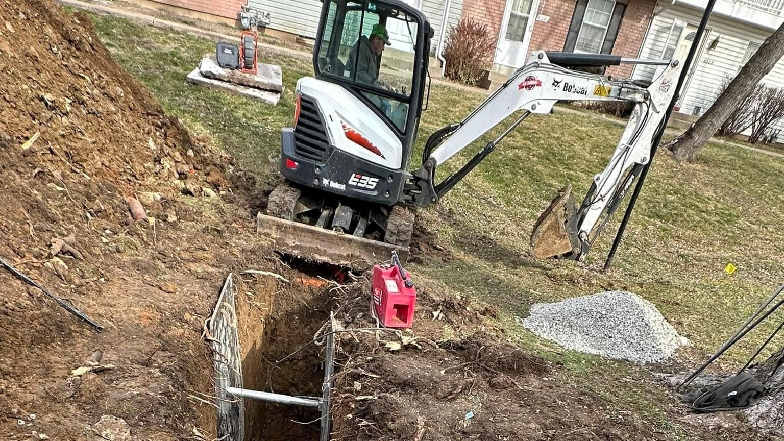 A small excavator is digging a hole in the ground in front of a house.