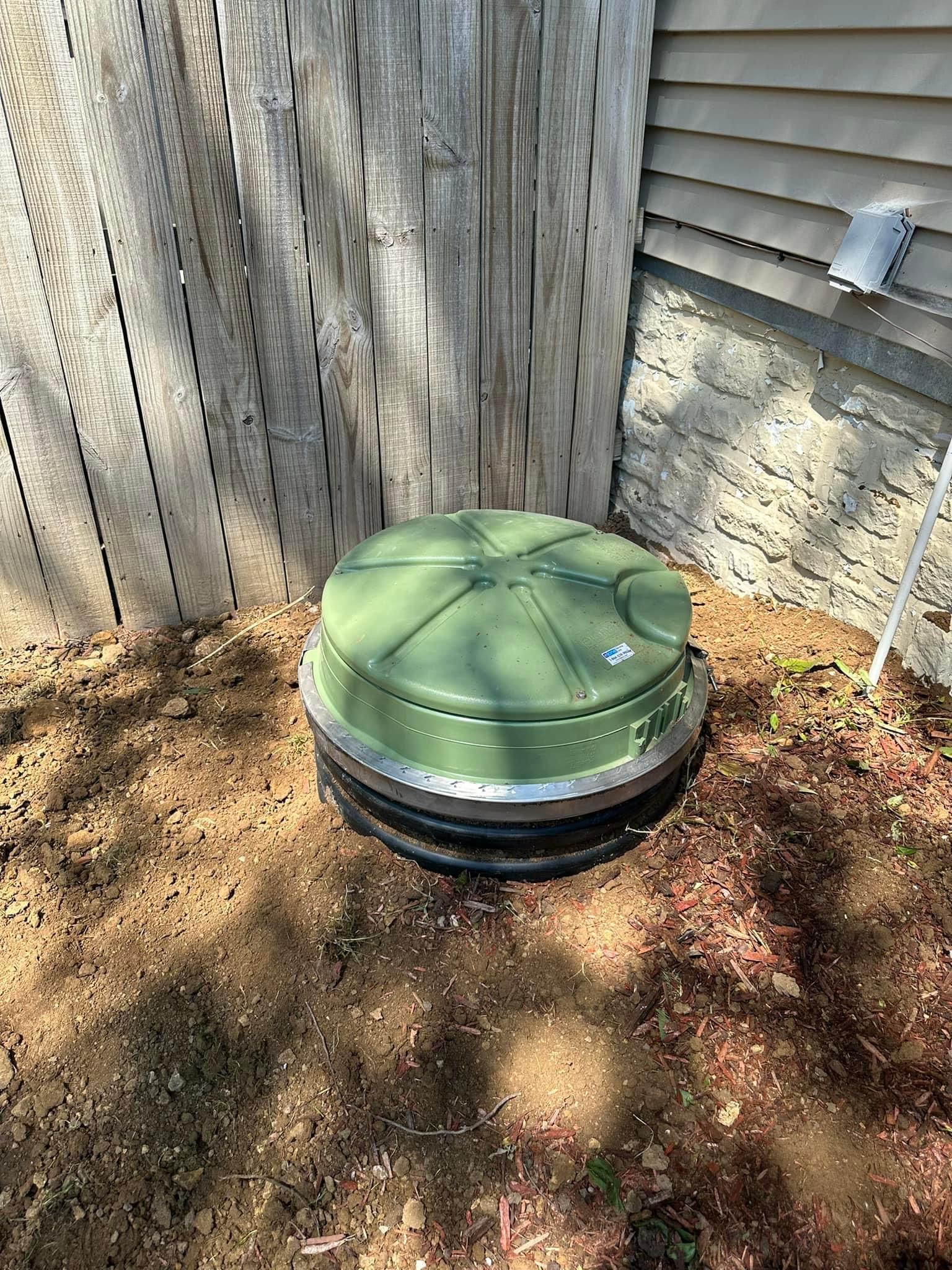 A green container is sitting in the dirt next to a wooden fence.