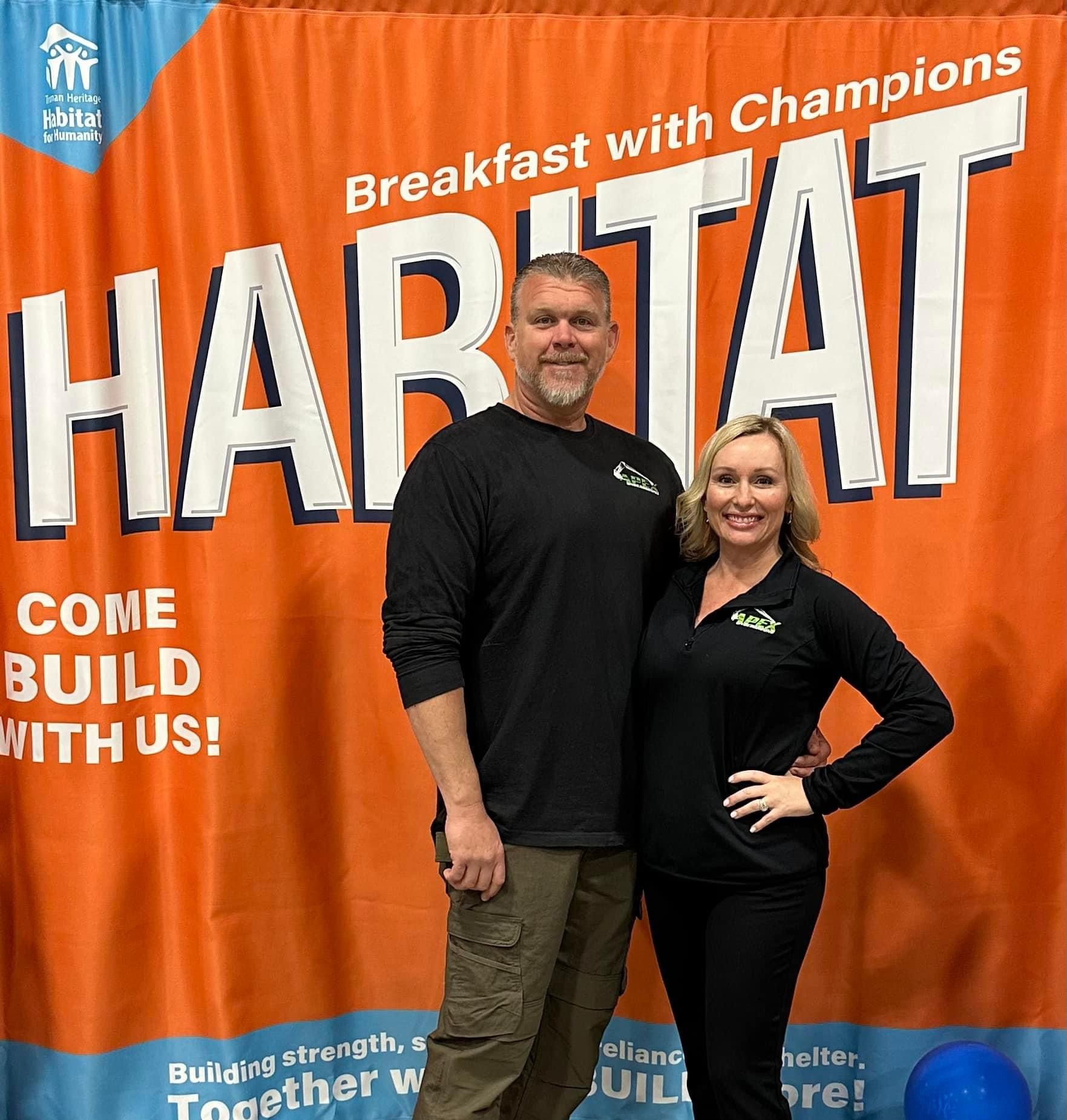 A man and a woman are standing in front of an orange curtain that says habitat.