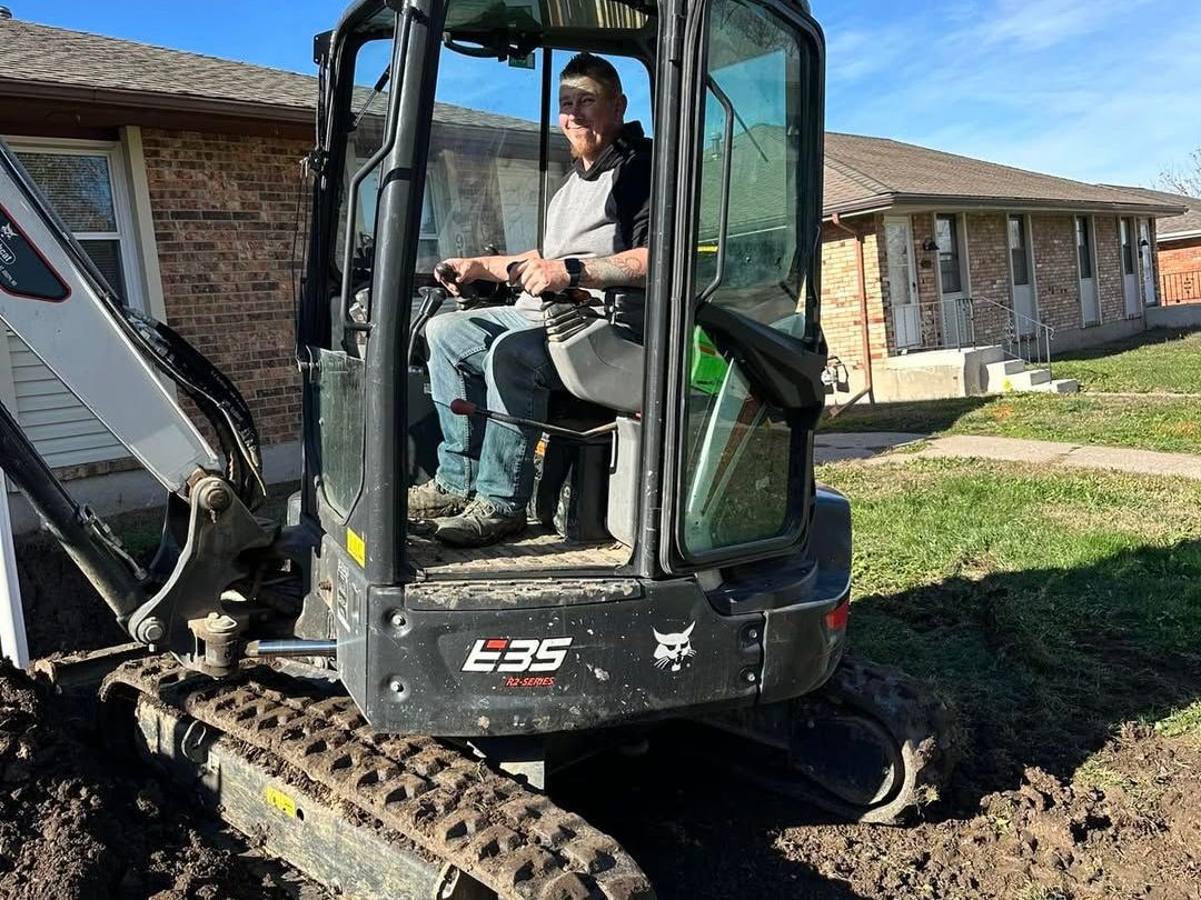 A man is driving a small excavator in front of a house.