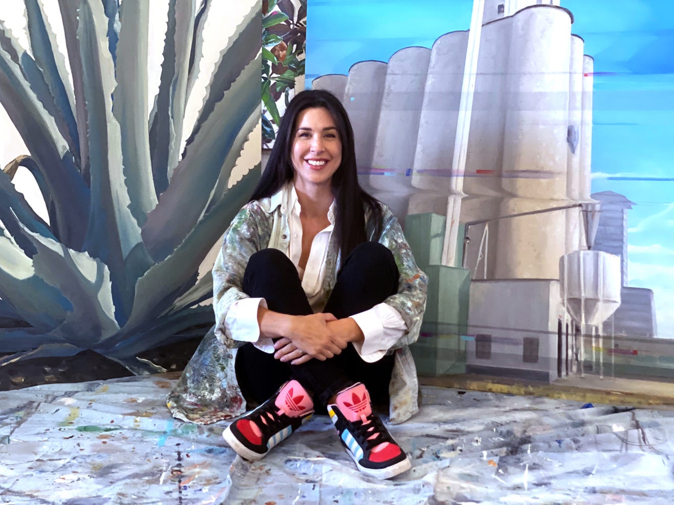 A woman is sitting on the floor in front of a painting.