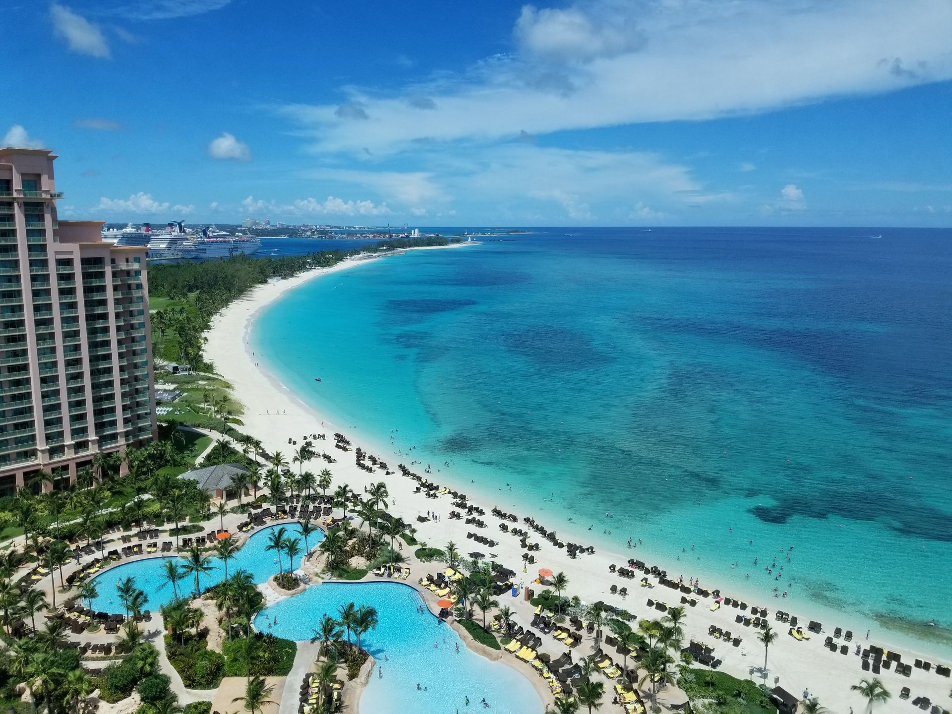 Beach with turquoise water, white sand, palm trees, resort building, and sunny sky.