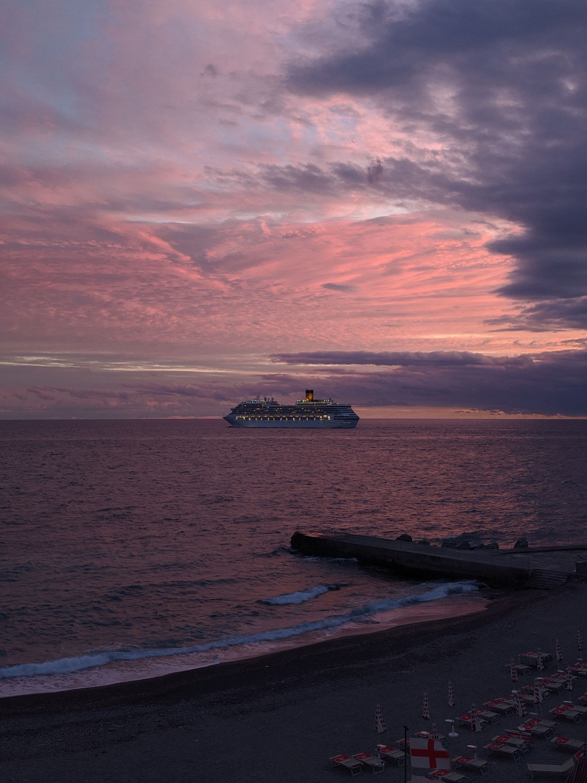 Ocean at dusk, with a cruise ship in the distance, under a pink and purple sky.