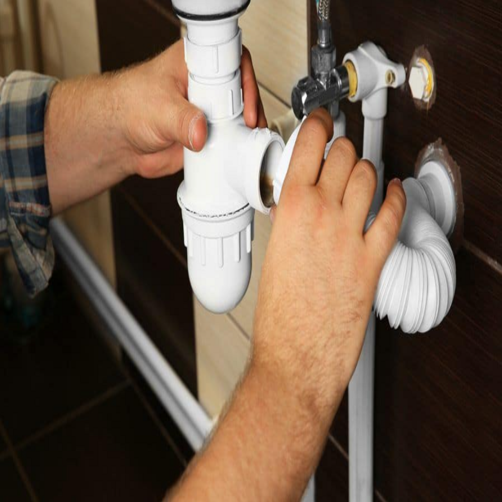 Person assembling white plumbing pipes under a sink.