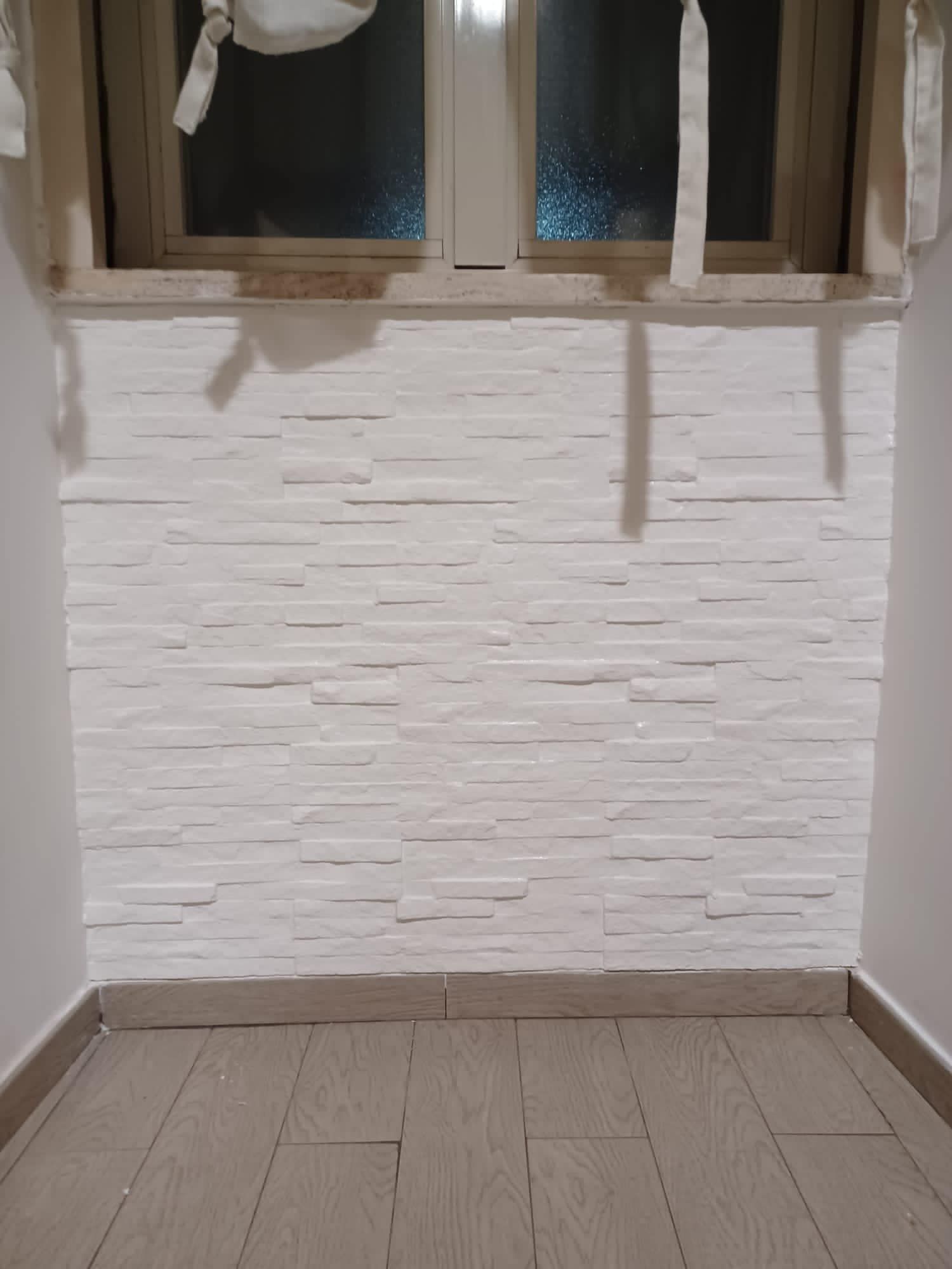 Una stanza con un muro di mattoni bianchi e una finestra.