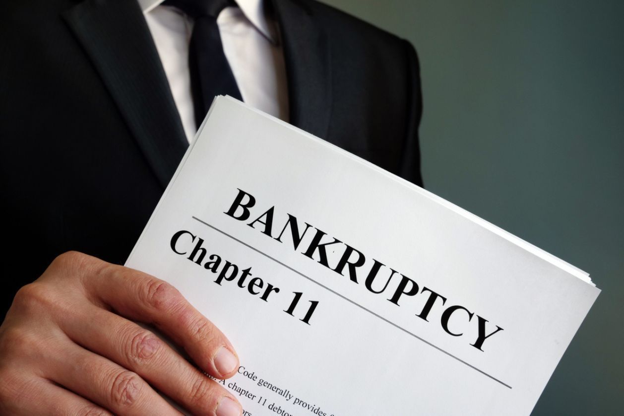A man in a suit and tie is holding a book titled bankruptcy chapter 11.