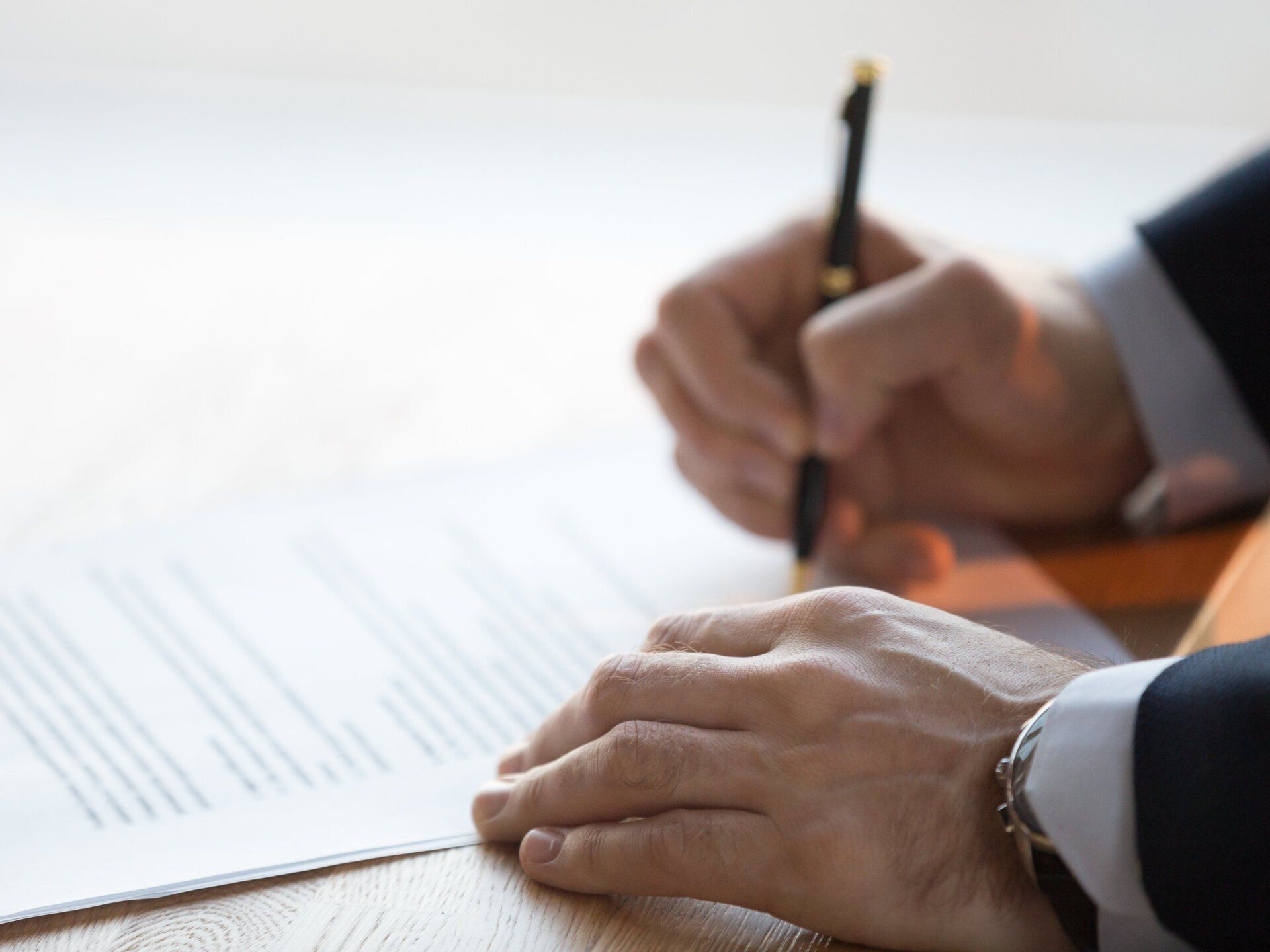 A man is writing on a piece of paper with a pen.