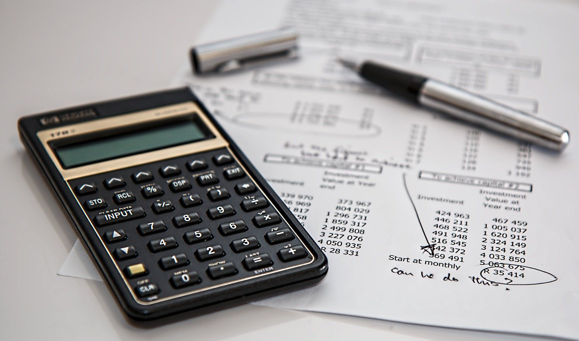 A calculator is sitting on top of a piece of paper next to a pen.