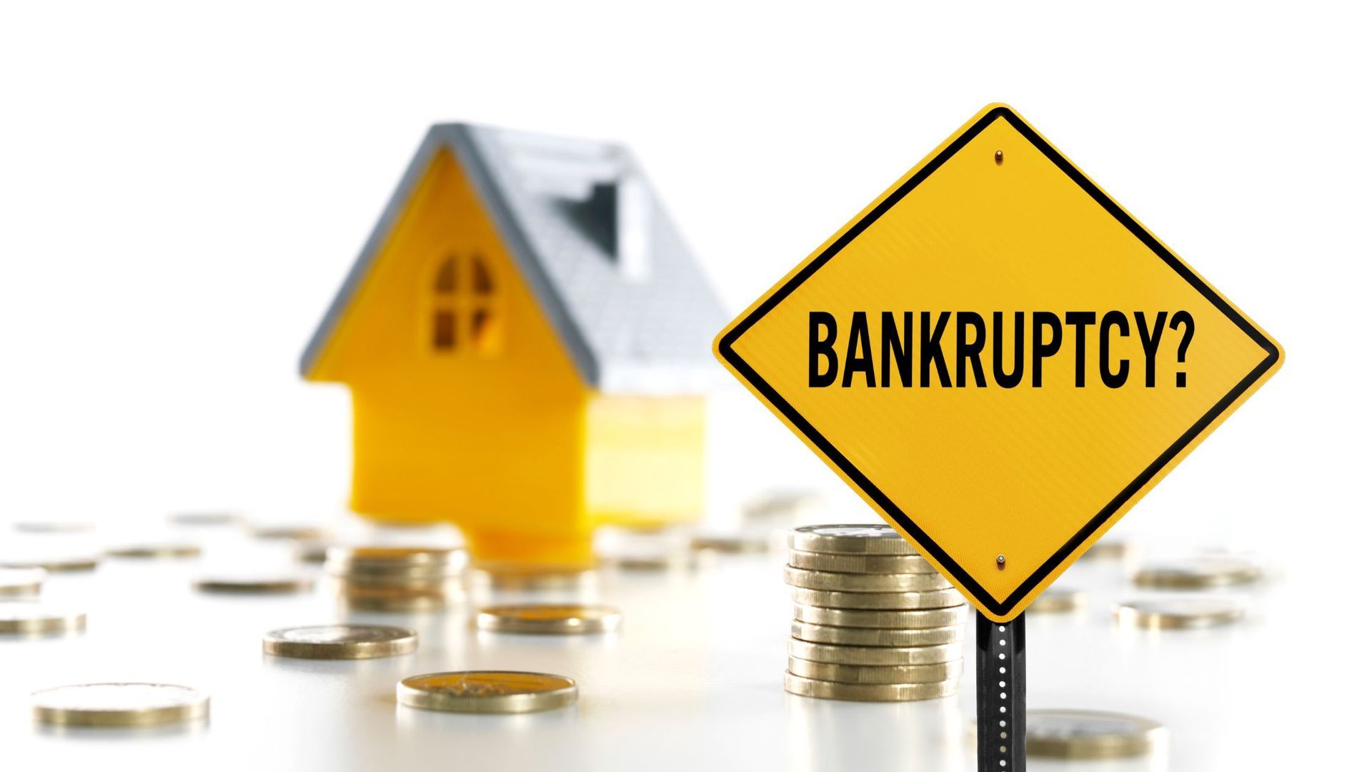 A yellow sign that says bankruptcy is next to a house and stacks of coins.