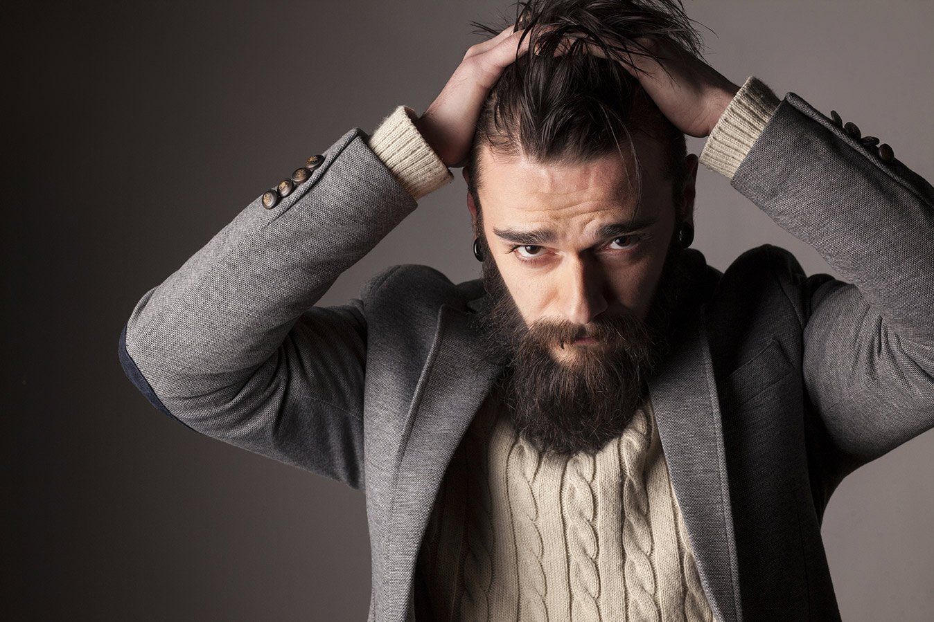 A man with a beard is holding his head with his hands.
