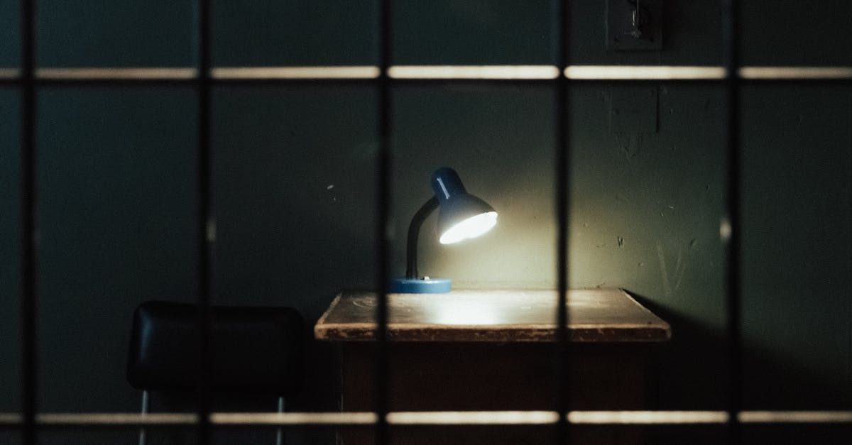 A lamp is sitting on a desk in a dark room behind bars.