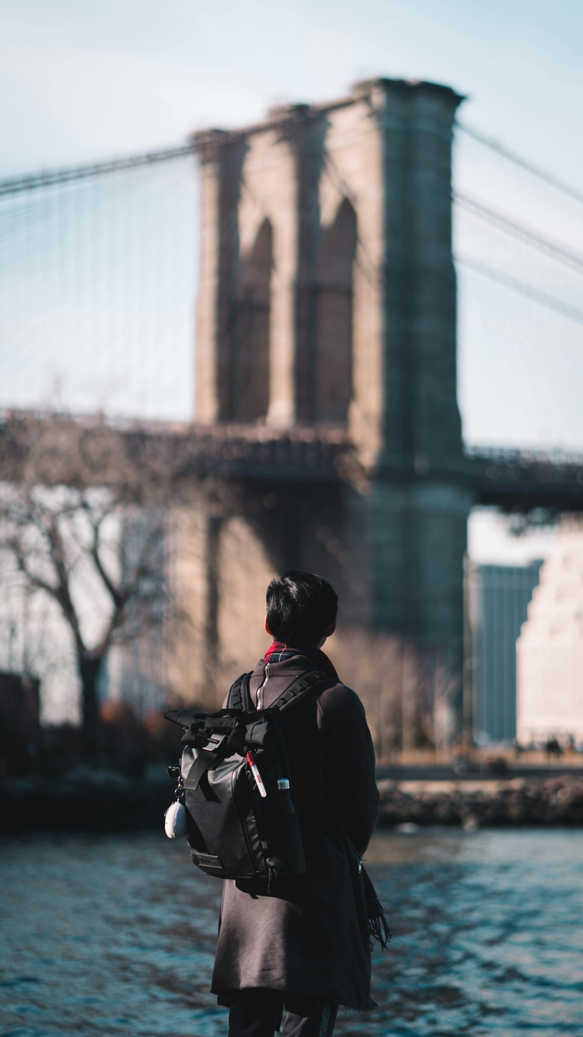 A man is standing in front of a bridge over a body of water.