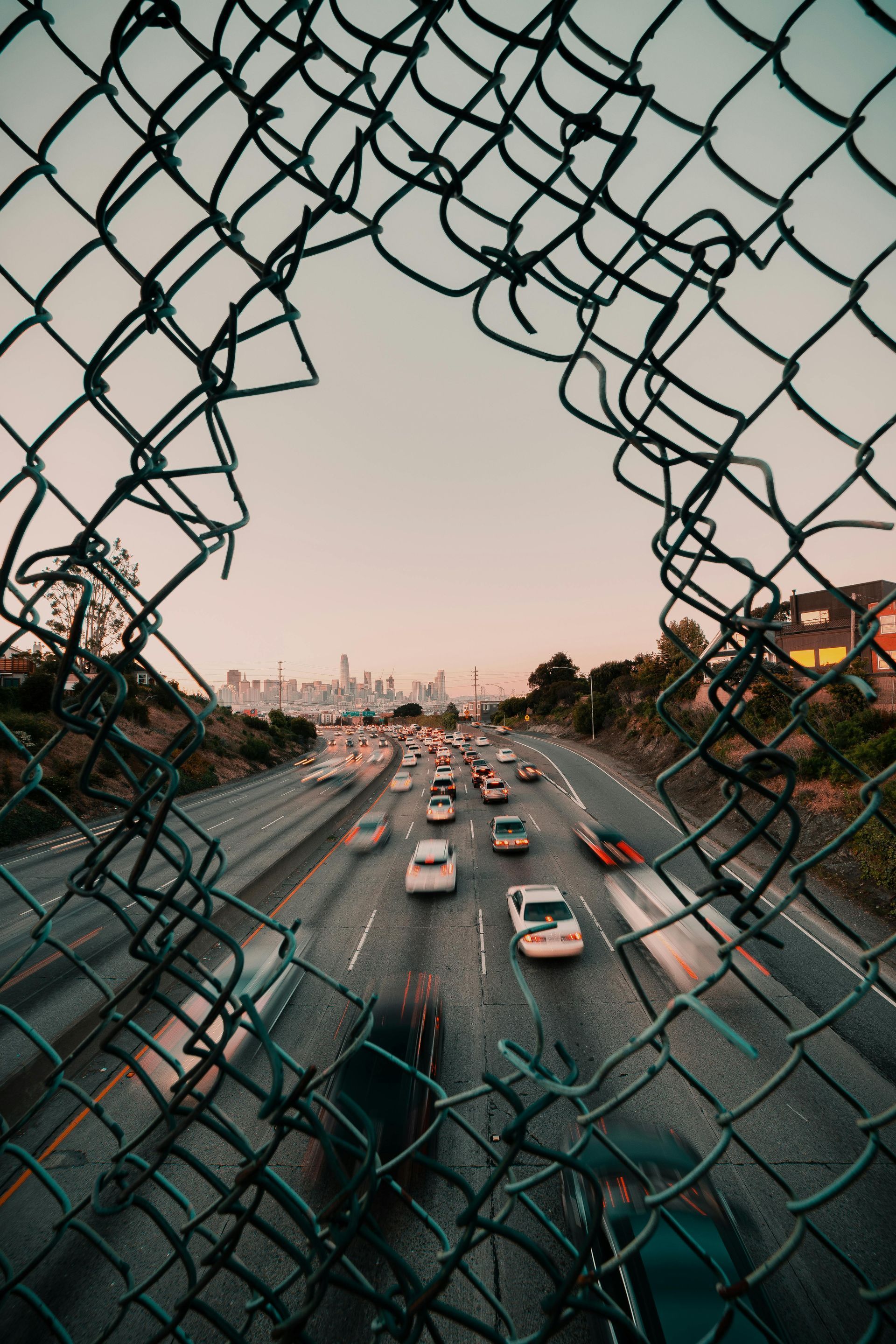 A view of a highway through a broken chain link fence.