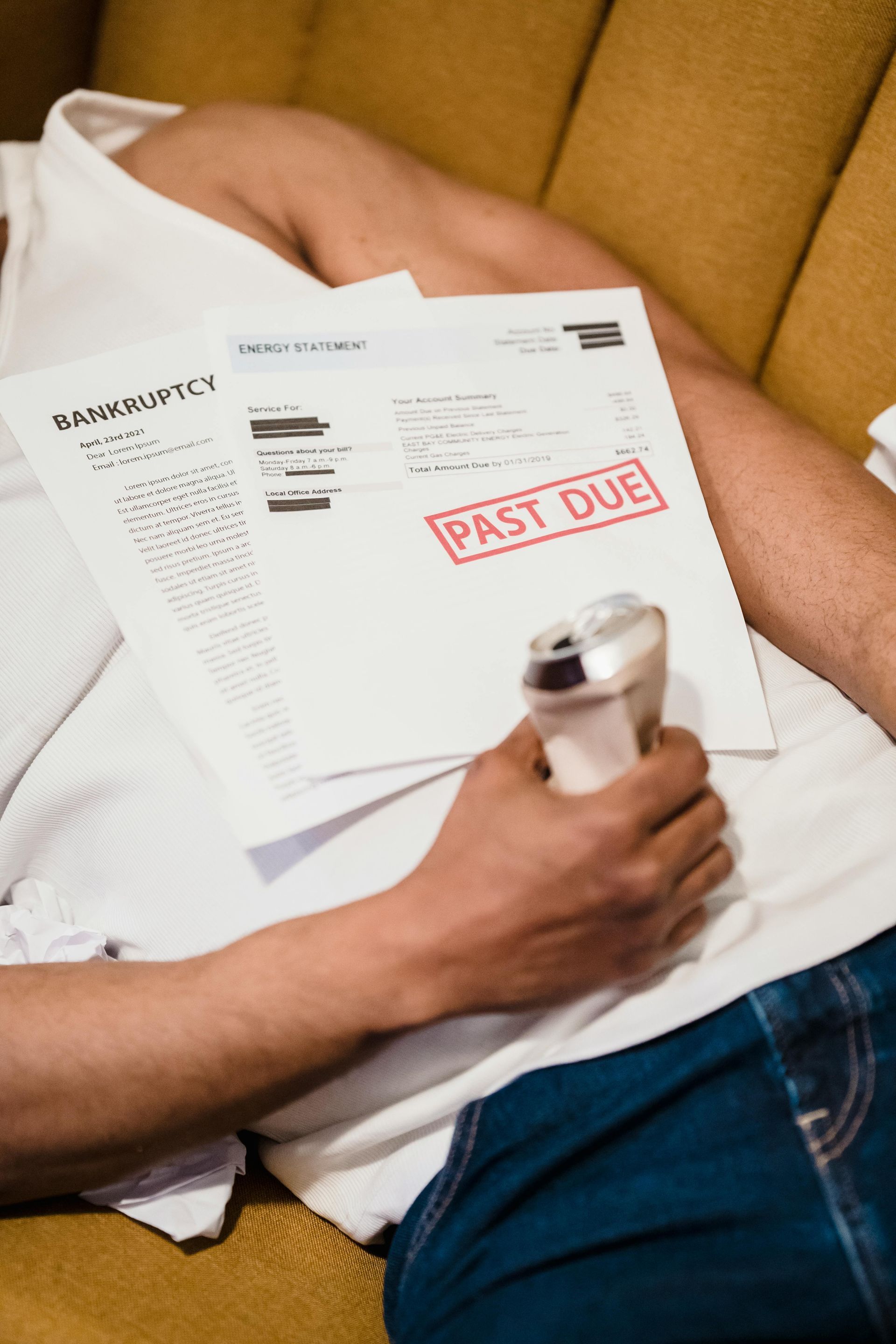 A man is laying on a couch holding papers and a cell phone.