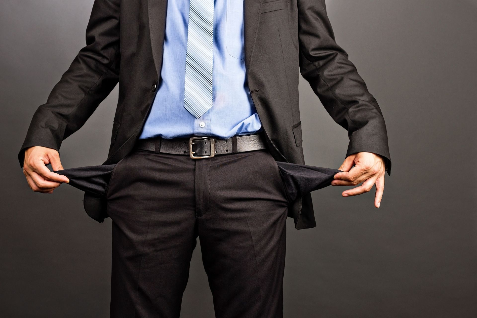 A man in a suit and tie is showing his empty pockets.