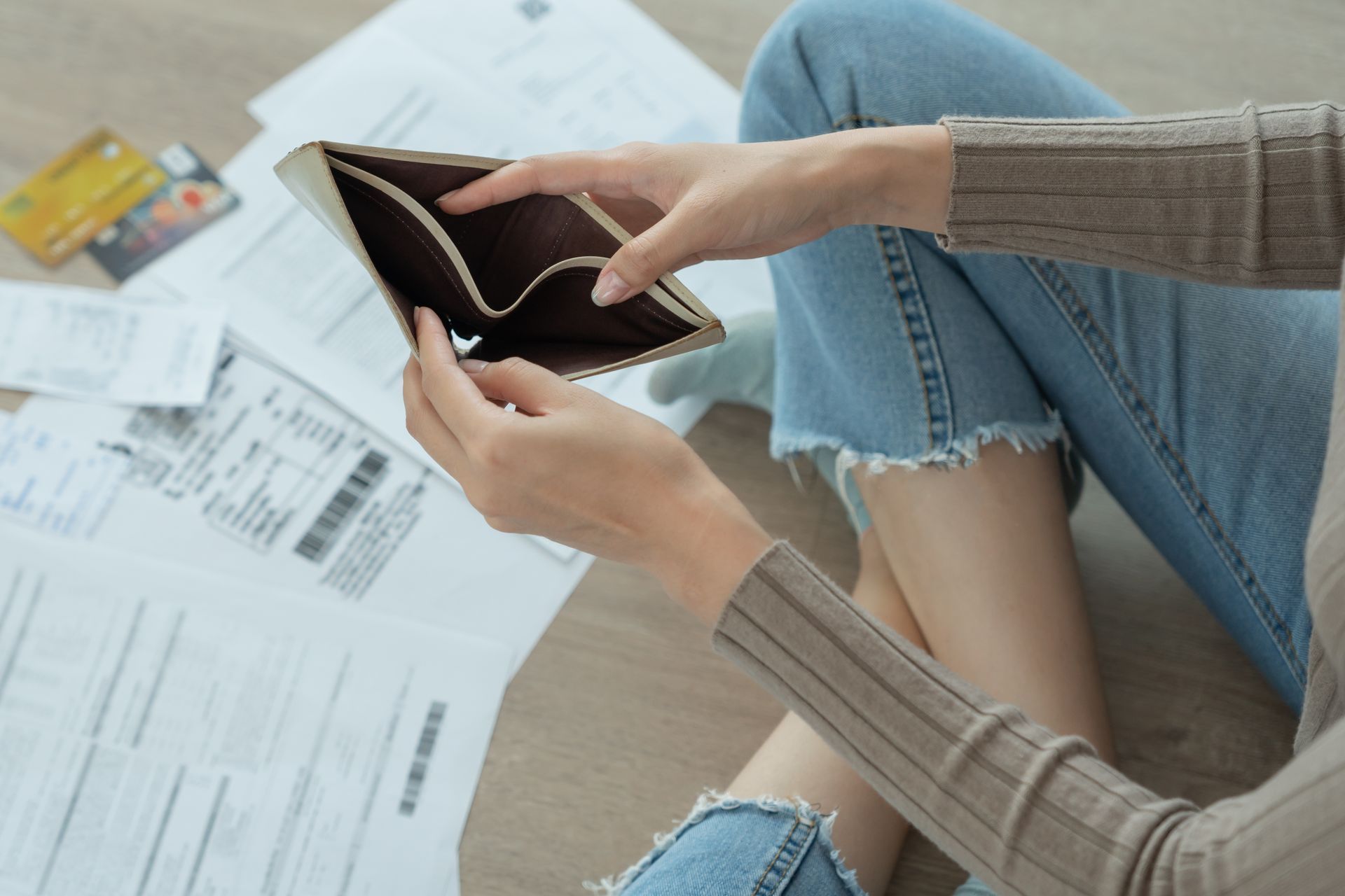 A woman is sitting on the floor holding an empty wallet.