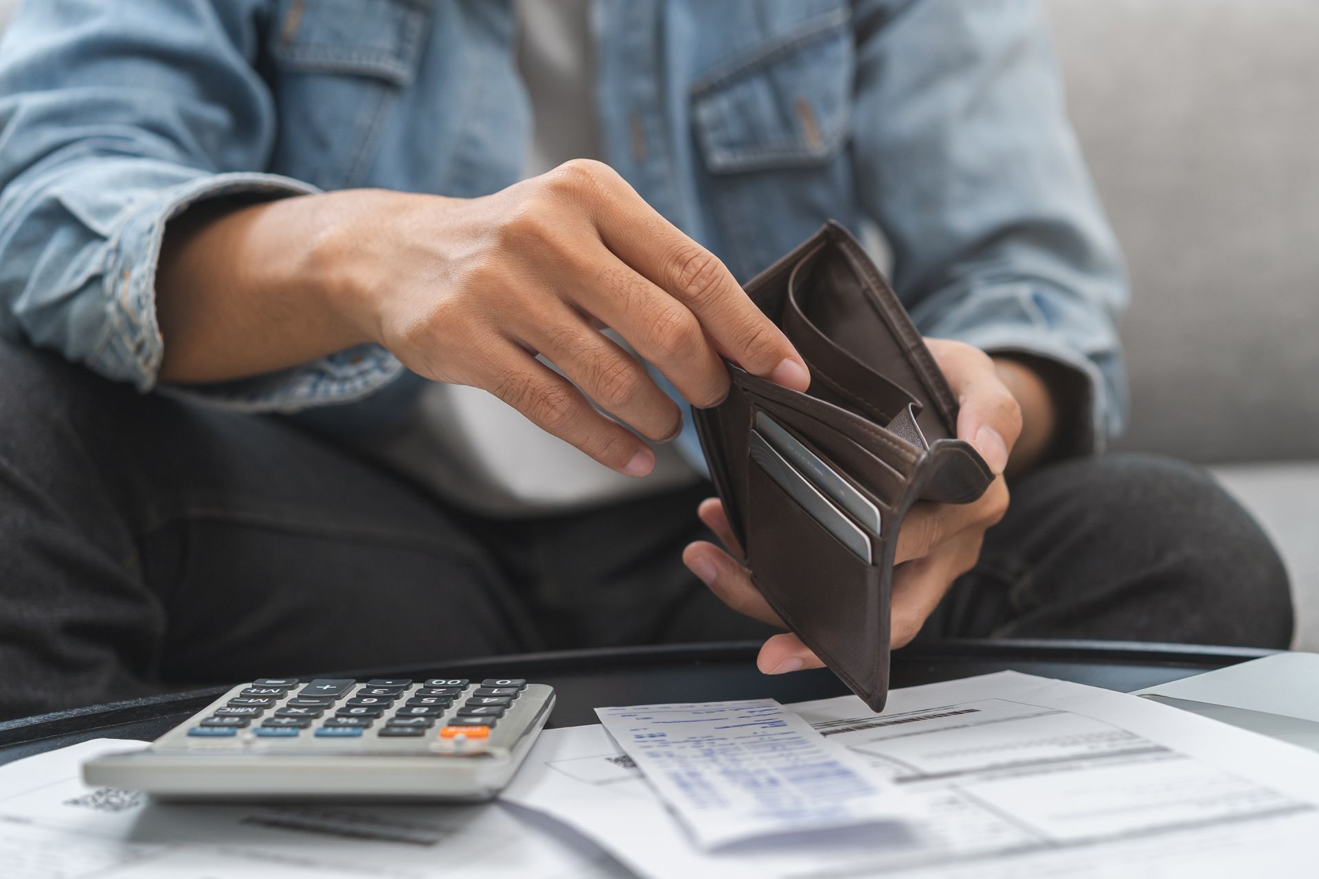 A man is sitting on a couch holding an empty wallet.