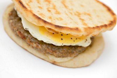 A close up of a sausage and egg sandwich on a white surface