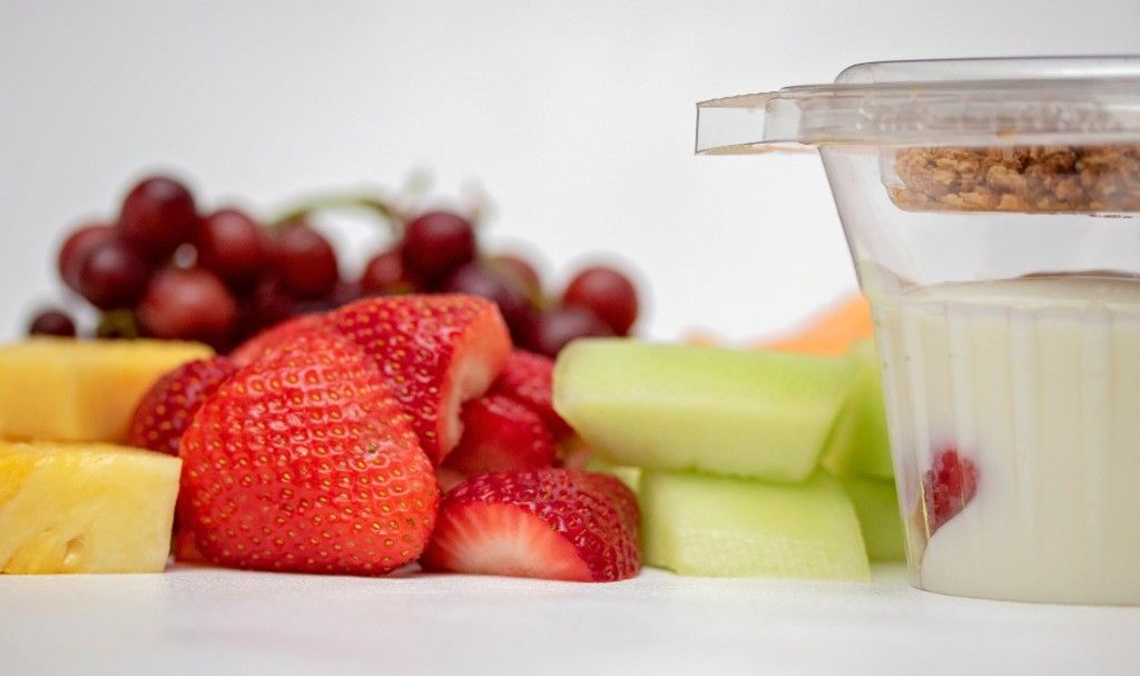 There is a container of yogurt next to a tray of fruit