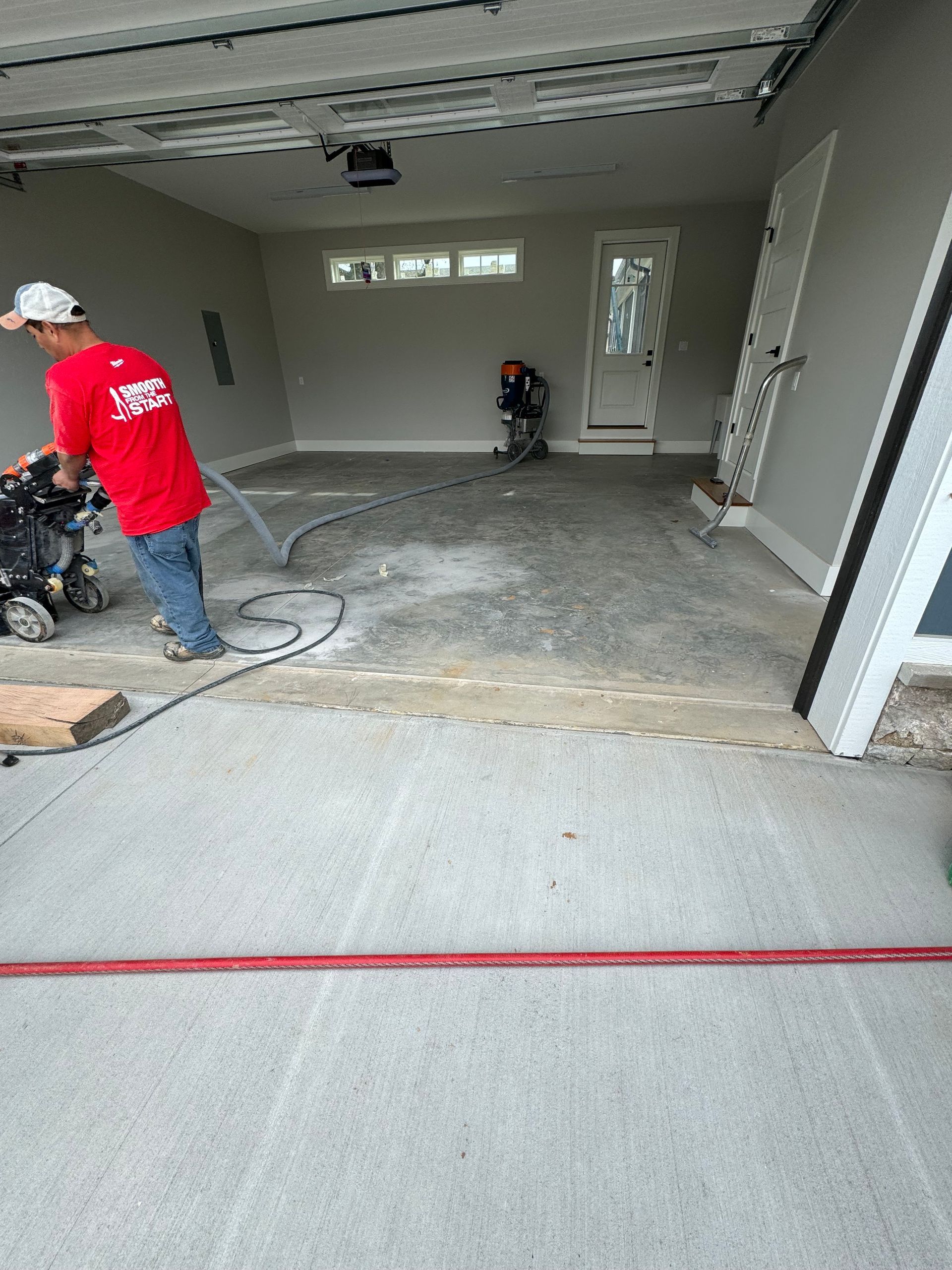 A man in a red shirt is cleaning a garage floor with a vacuum cleaner.
