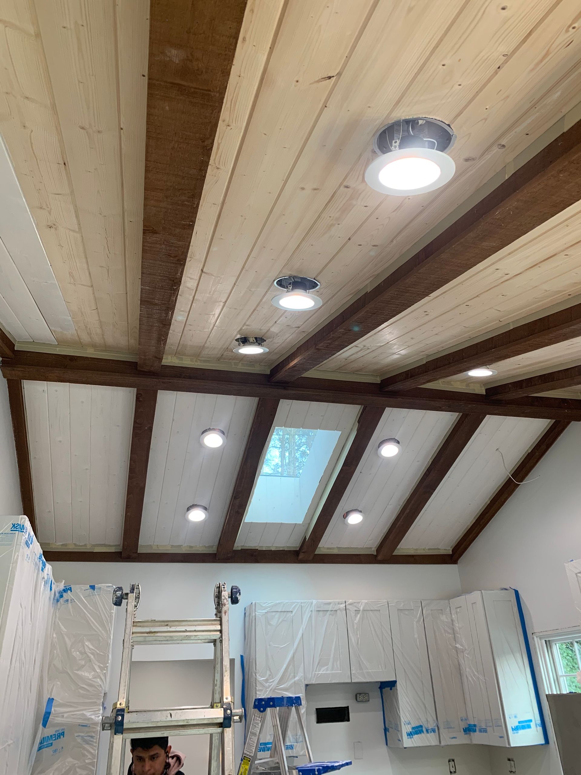 A man is standing on a ladder in a kitchen with a wooden ceiling.
