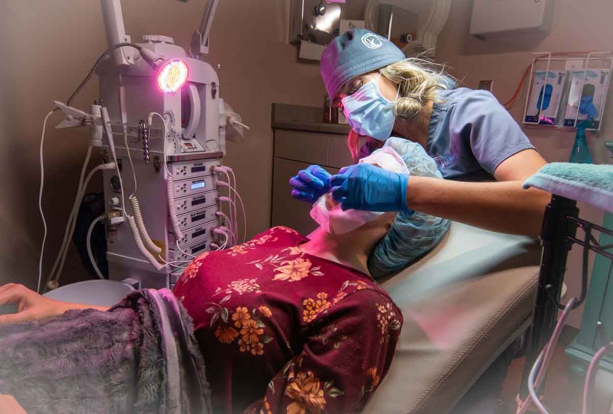 Medical personnel performing a procedure on a patient lying on a bed in a medical setting.