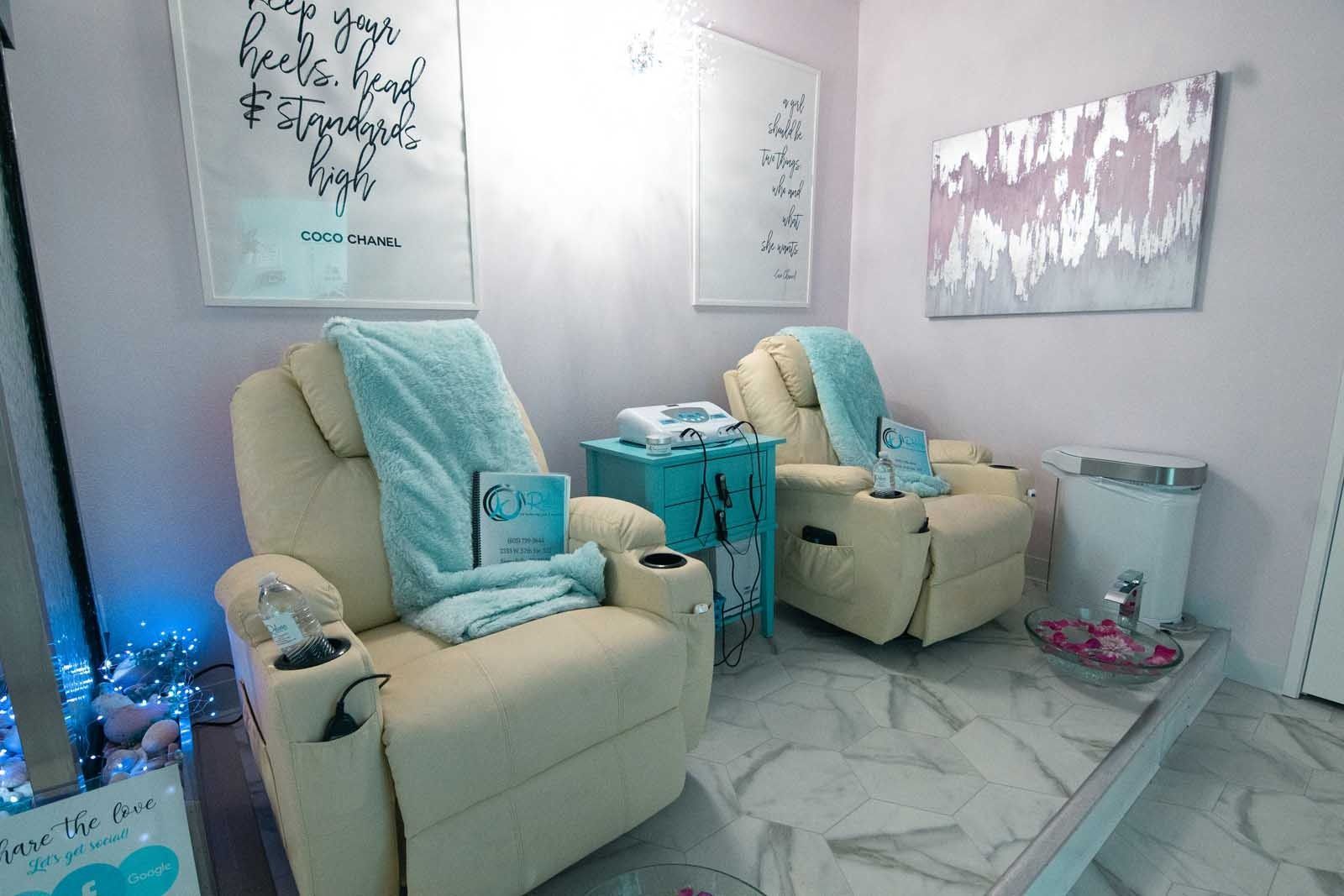Two beige recliners in a spa-like room with light blue towels, artwork, and a small table.