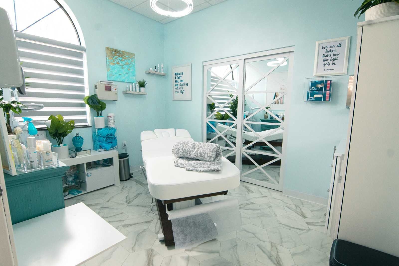 Spa treatment room, light blue walls, massage table, sliding door to a second room, white marble floor.