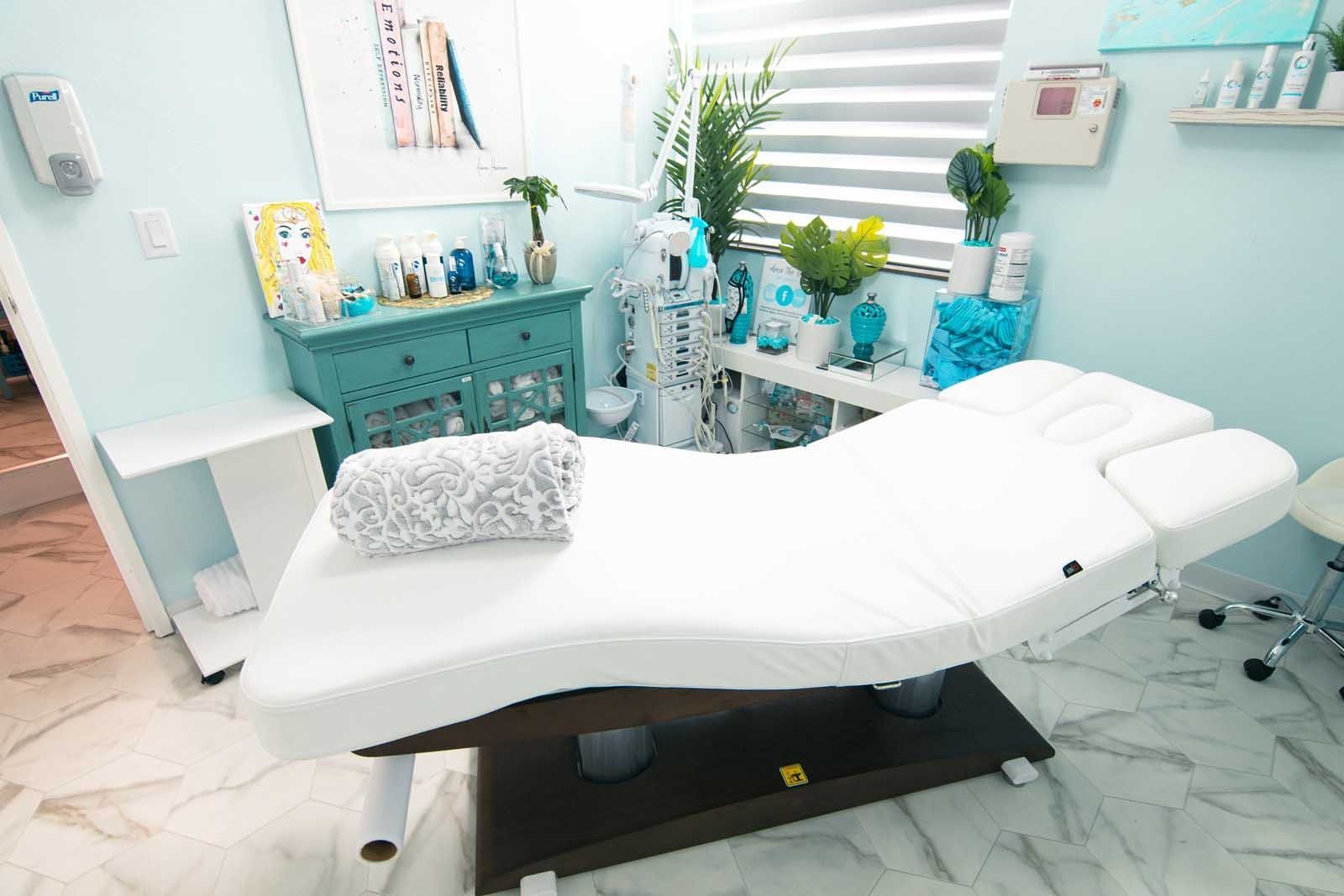 Treatment room with white bed, turquoise accents, medical equipment, and plants.