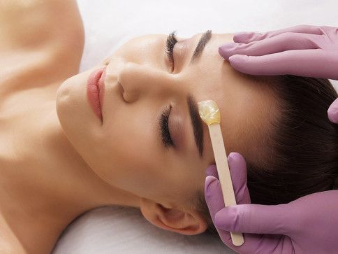 Person receiving eyebrow waxing treatment; close-up with gloved hands applying wax.