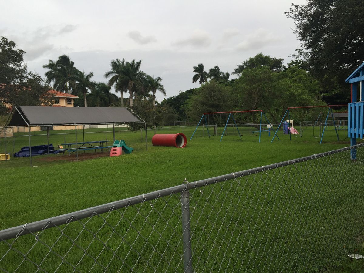 A chain link fence surrounds a lush green playground