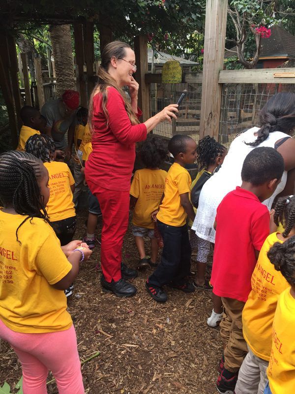 A woman in a red shirt is talking to a group of children in yellow shirts.