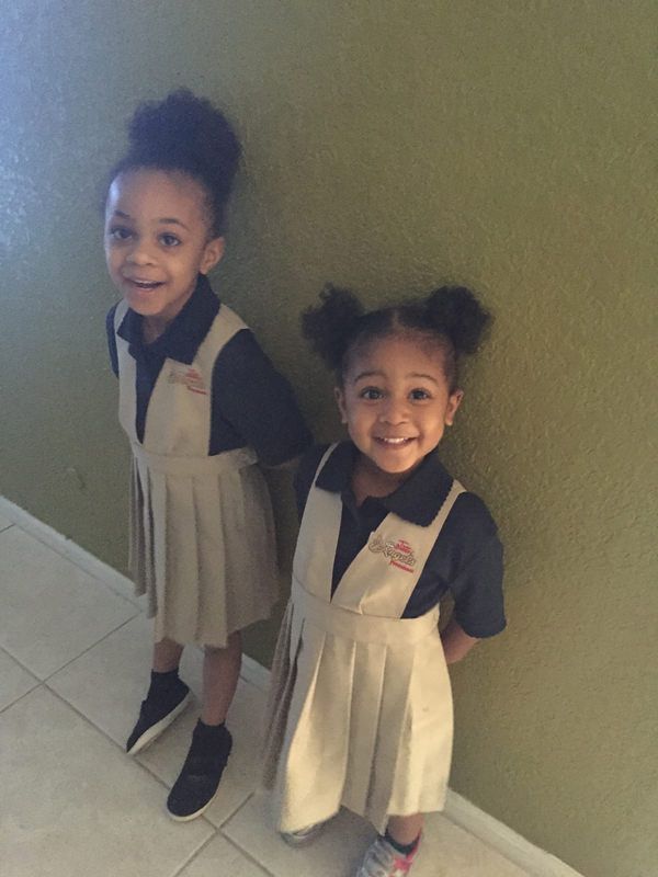 Two little girls wearing school uniforms are standing next to each other