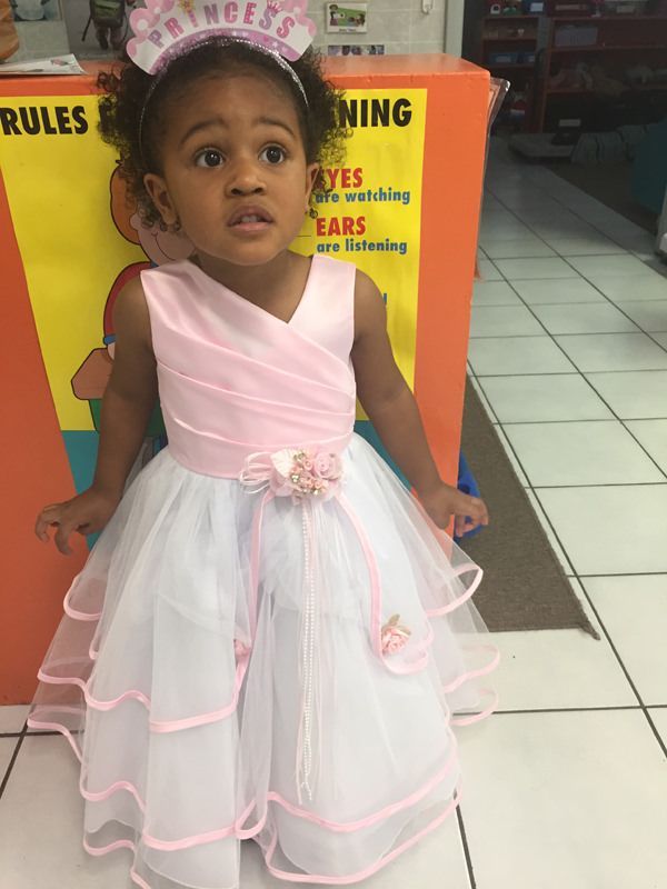 A little girl wearing a pink and white dress and tiara