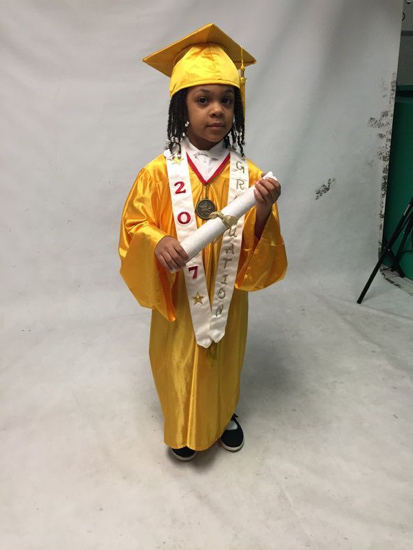 A little girl in a graduation cap and gown is holding a diploma